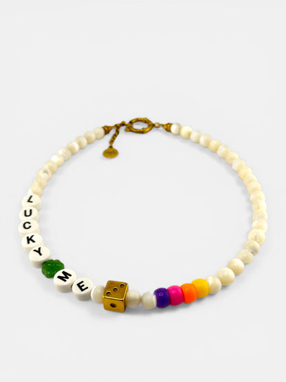 Vue de dessus du collier Lucky Dice Bingo Club posé à plat sur un fond blanc texturé. La chaîne dorée de 40 cm est disposée en cercle, avec le dé doré et le trèfle émaillé vert positionnés au centre inférieur. Le fermoir mousqueton est visible à l'opposé. Composition épurée et lumineuse.
