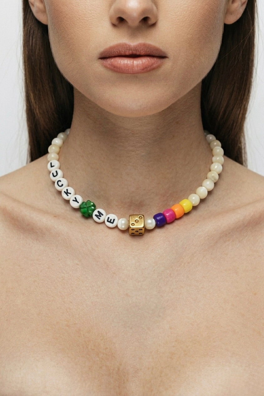 Plan rapproché du collier Lucky Dice Bingo Club porté au cou d'une femme. La chaîne fine dorée met en valeur le pendentif dé doré texturé et le trèfle à quatre feuilles émaillé vert. Le collier repose sur la peau nue, entre les clavicules. Éclairage doux et naturel.