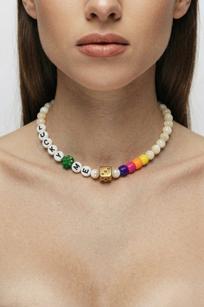 Plan rapproché du collier Lucky Dice Bingo Club porté au cou d'une femme. La chaîne fine dorée met en valeur le pendentif dé doré texturé et le trèfle à quatre feuilles émaillé vert. Le collier repose sur la peau nue, entre les clavicules. Éclairage doux et naturel.