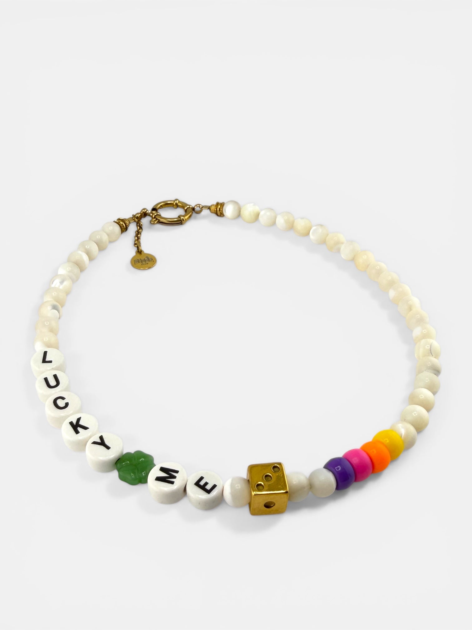 Le collier Lucky Dice Bingo Club. Le pendentif dé doré et le trèfle vert apportent une touche de couleur et de fantaisie chic à la tenue sobre. L'image inspire un look 'bohème sophistiqué'. Éclairage d'ambiance chaleureux.