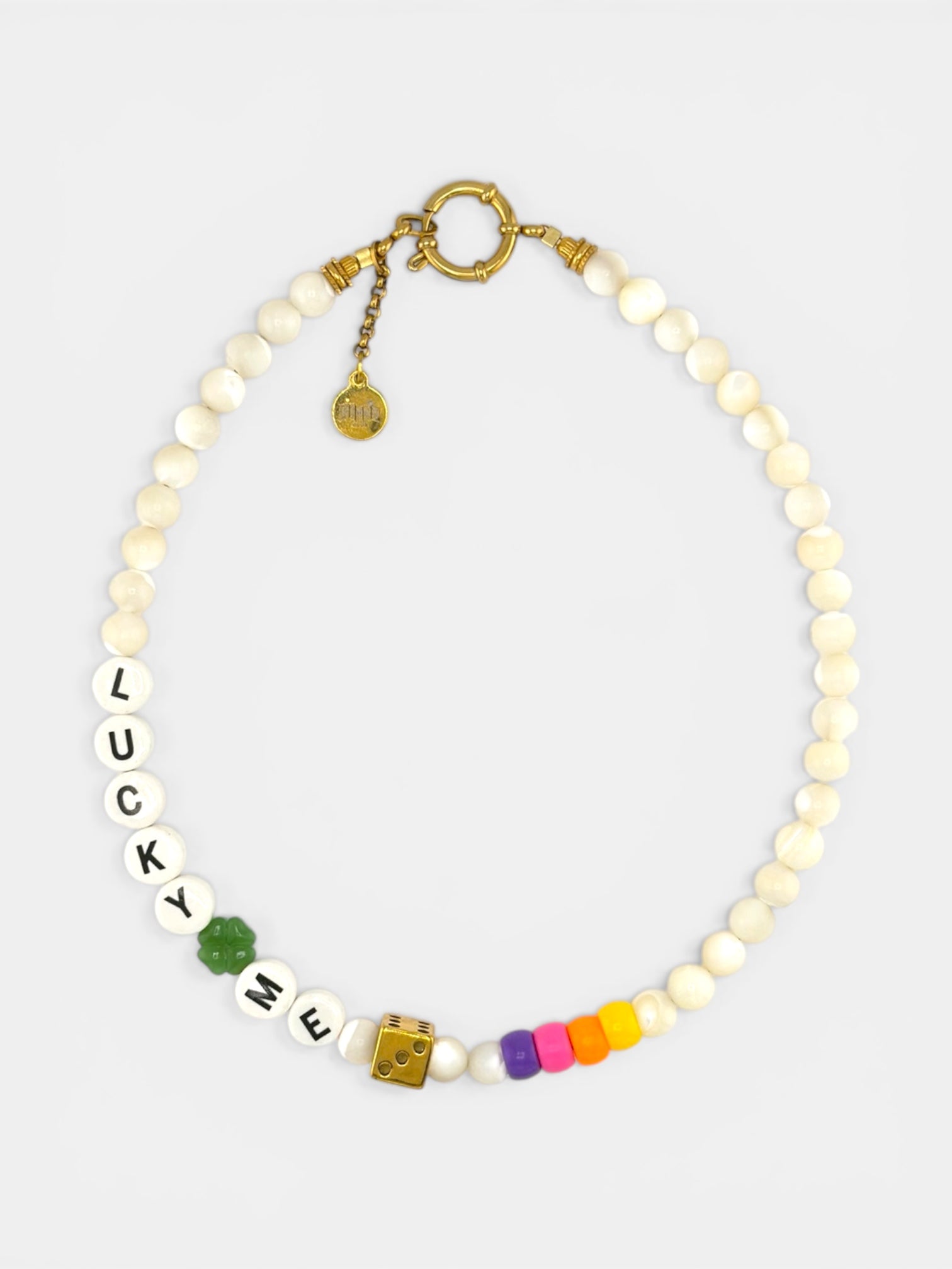 Gros plan détaillé sur les pendentifs du collier Lucky Dice. On distingue nettement le dé en laiton texturé doré et le trèfle à quatre feuilles en émail vert brillant. Les pendentifs sont suspendus à la chaîne fine en acier inoxydable plaqué or 18k. Mise au point nette sur les détails métalliques.